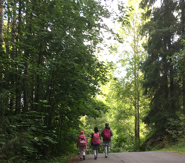 Kolme tyttöä kävelemässä metsäisellä tiellä.