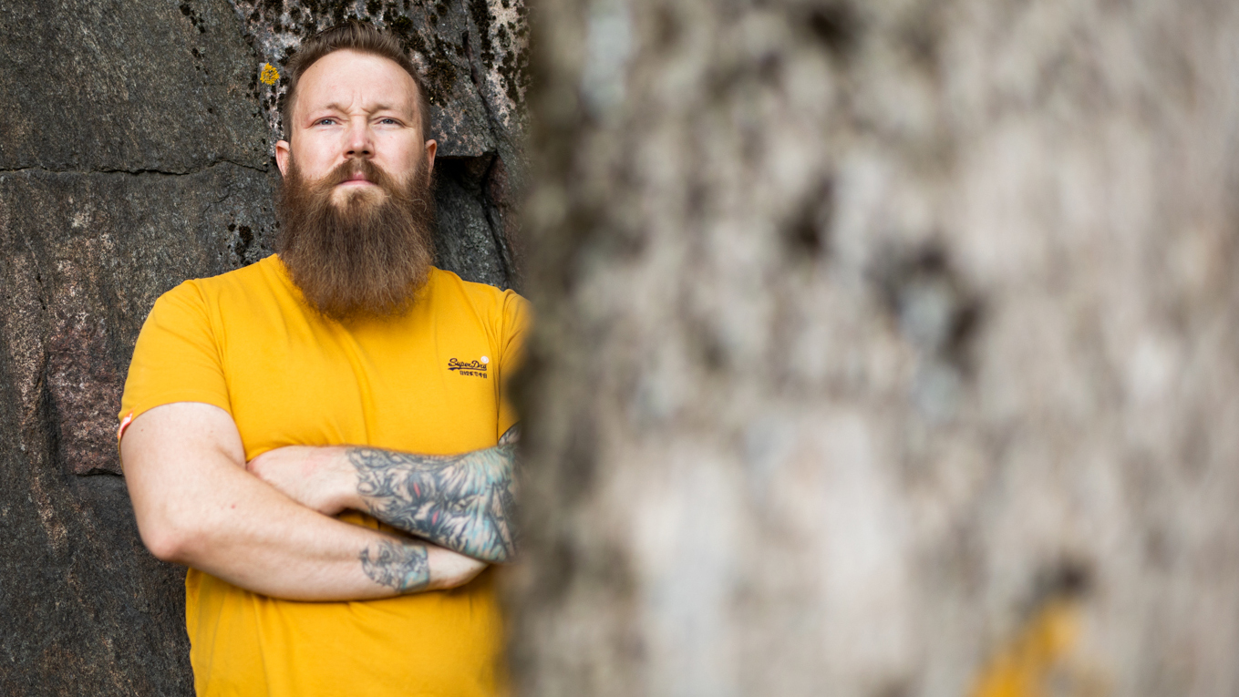 En man tittar på kameran, delvis bakom ett träd.