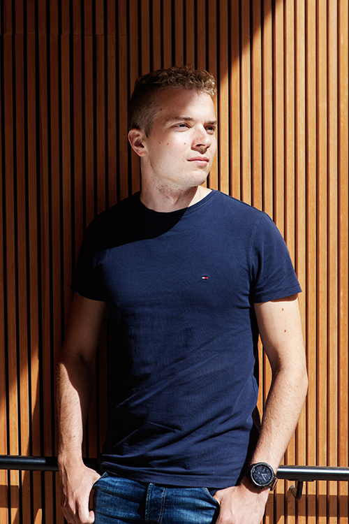 Mies poseeraa puupaneeliseinän edessä.