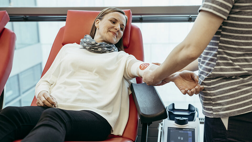 Hoitaja tekee naiselle verenluovutuksen jälkeen siteen kyynärtaipeeseen.