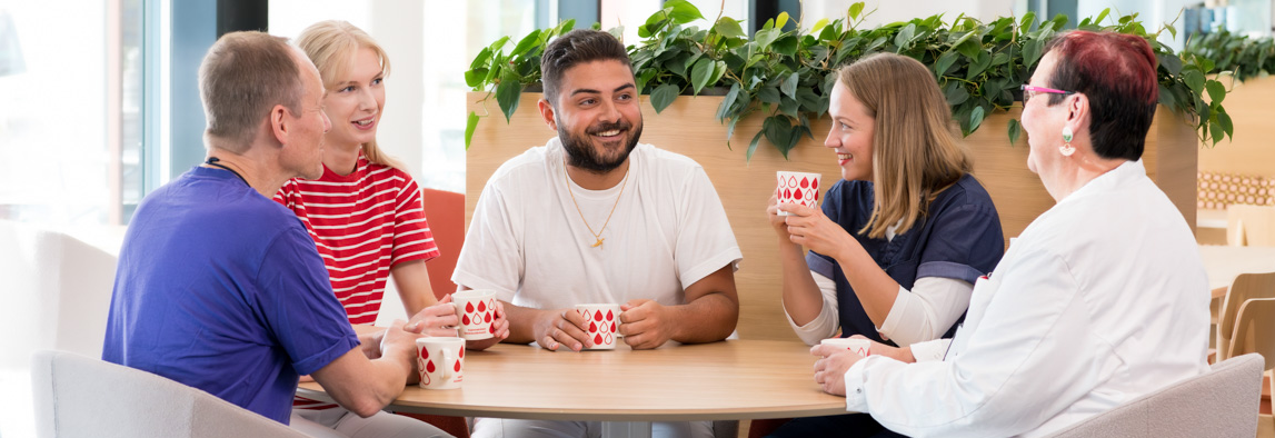 Veripalvelun työntekijöitä ruokapöydän ympärillä.
