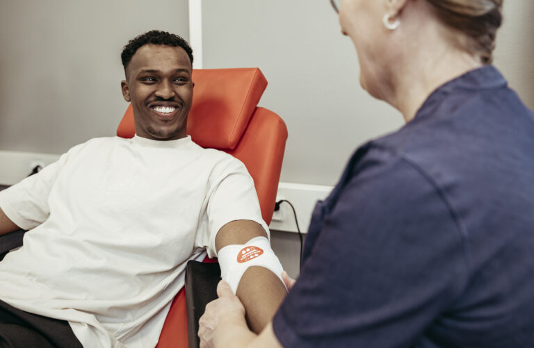The blood donor smiles at the nurse who is putting on the bandage after the donation.