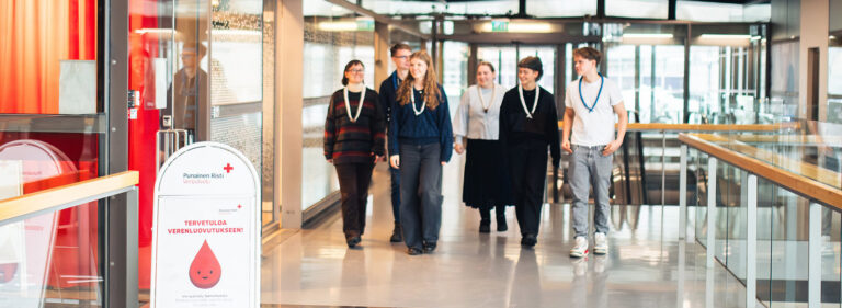 A group of scouts walks down the corridor towards the camera, with a sign in the foreground saying Welcome to blood donation.