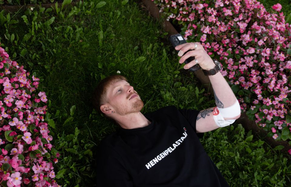 Mies makaa nurmikolla ja katsoo puhelinta hengenpelastaja-paita päällä.