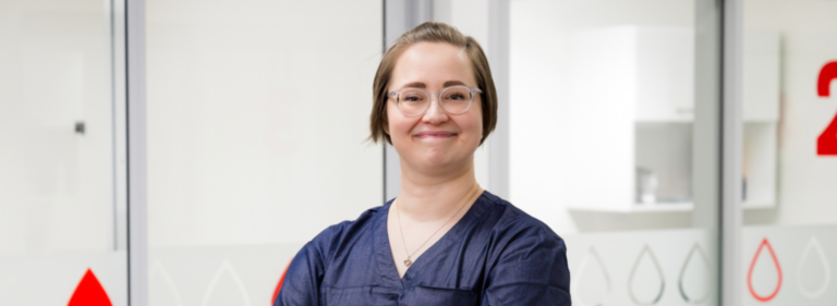 Henkilö seisoo vaaleaa taustaa vasten ja hymyilee kameralle.