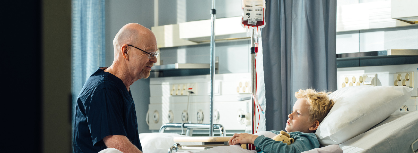 Potilas sairaalasängyssä hoitohenkilö vierellään.