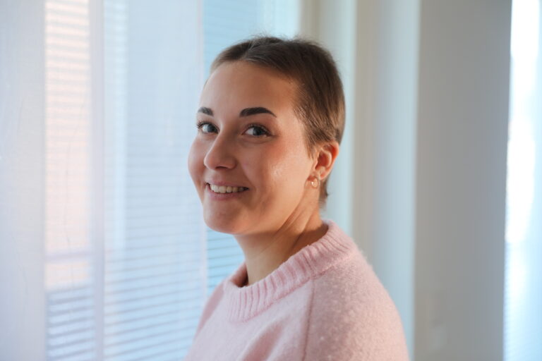 Nuori nainen, jolla lyhyt tykka, hymyilee kameralla vaaleaa taustaa vasten.