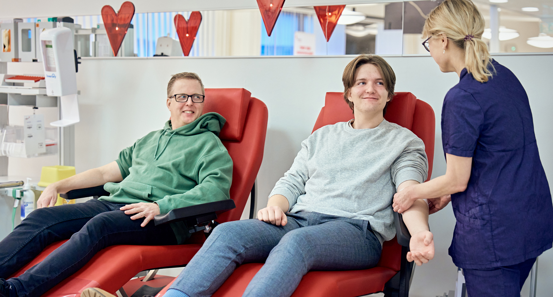 Kaksi verenluovuttajaa ja hoitaja verenluovutuspisteellä.