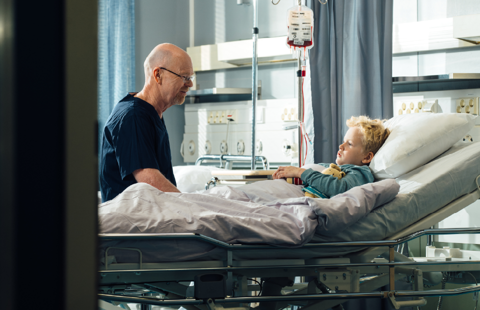 Lapsi potilasvuoteella hoitaja istuu vieressä.