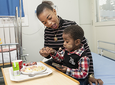 Emille's mother Anifa feeding the small patient in a hospital room.