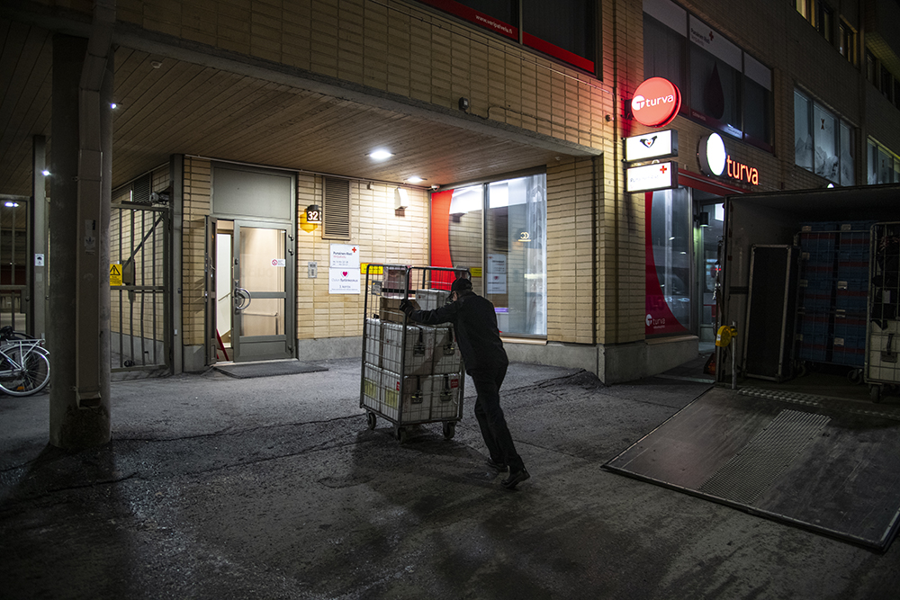 Liikkuvan Veripalvelun kuljettaja Markku purkamassa kuormaa iltahämärässä. Kuormassa on luovutettua verta sisältäviä kylmälaukkuja.
