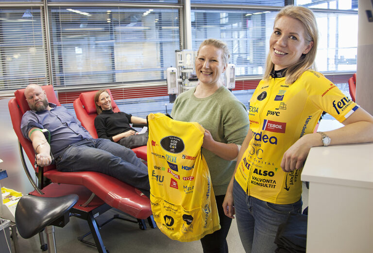 Två medlemmar i Team Rynkeby i förgrunden vid blodgivningsplats. Två blodgivare i bakgrunden. Fram till vänster Maria Salminen, höger Laura Suominen.