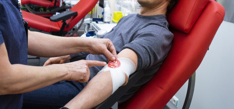 Hoitaja viimeistelemässä verenluovuttajan sidosta Hengenpelastajatarralla.