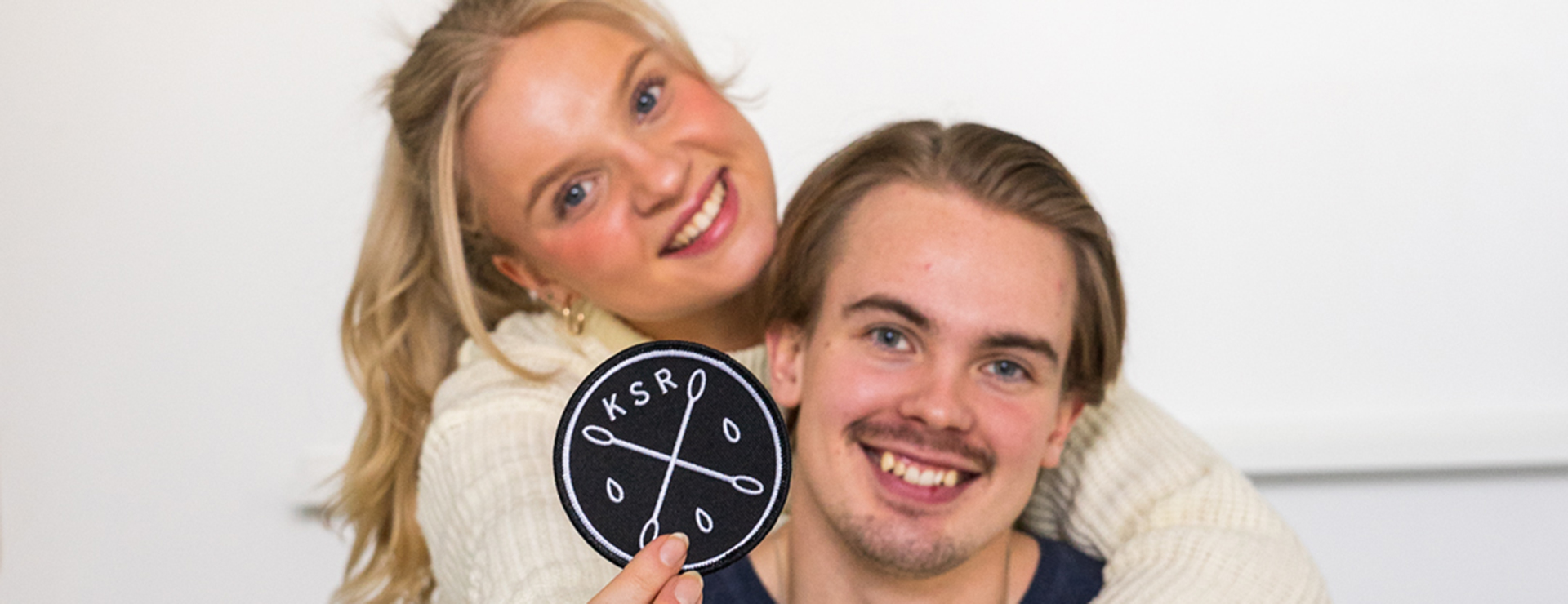 Two people look at the camera, smiling, one of them showing a stem cell registry fabric badge.