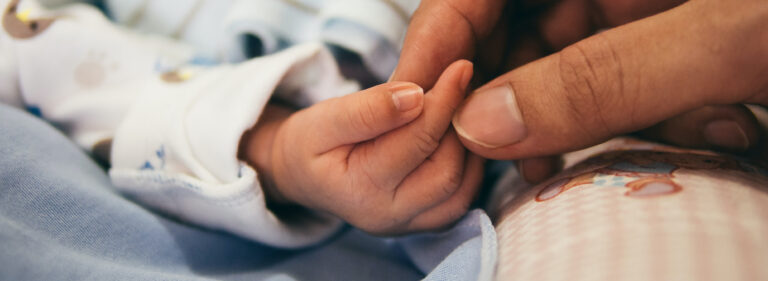 Aikuinen pitämässä kiinni pienen vauvan kädestä.