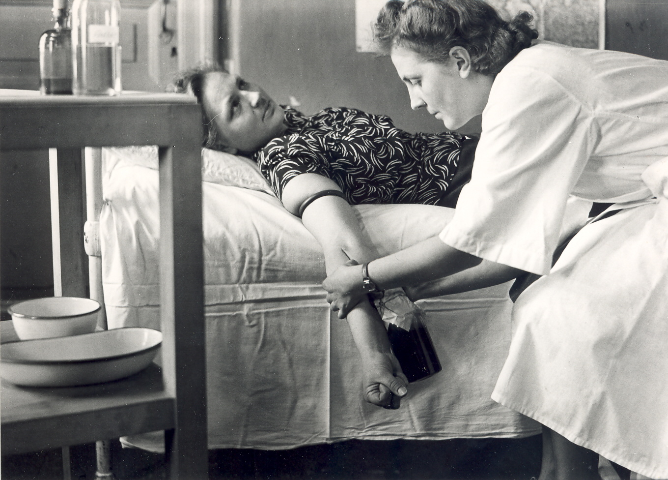 A picture from 1944, where blood is poured into a bottle directly from a donor lying on a bed.