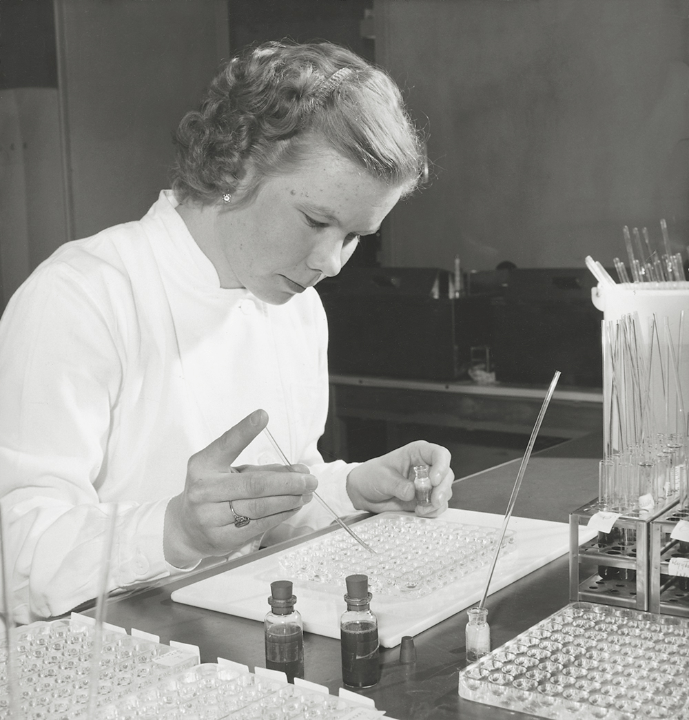 A black and white photo of a woman doing a manual blood type testing in 1960.