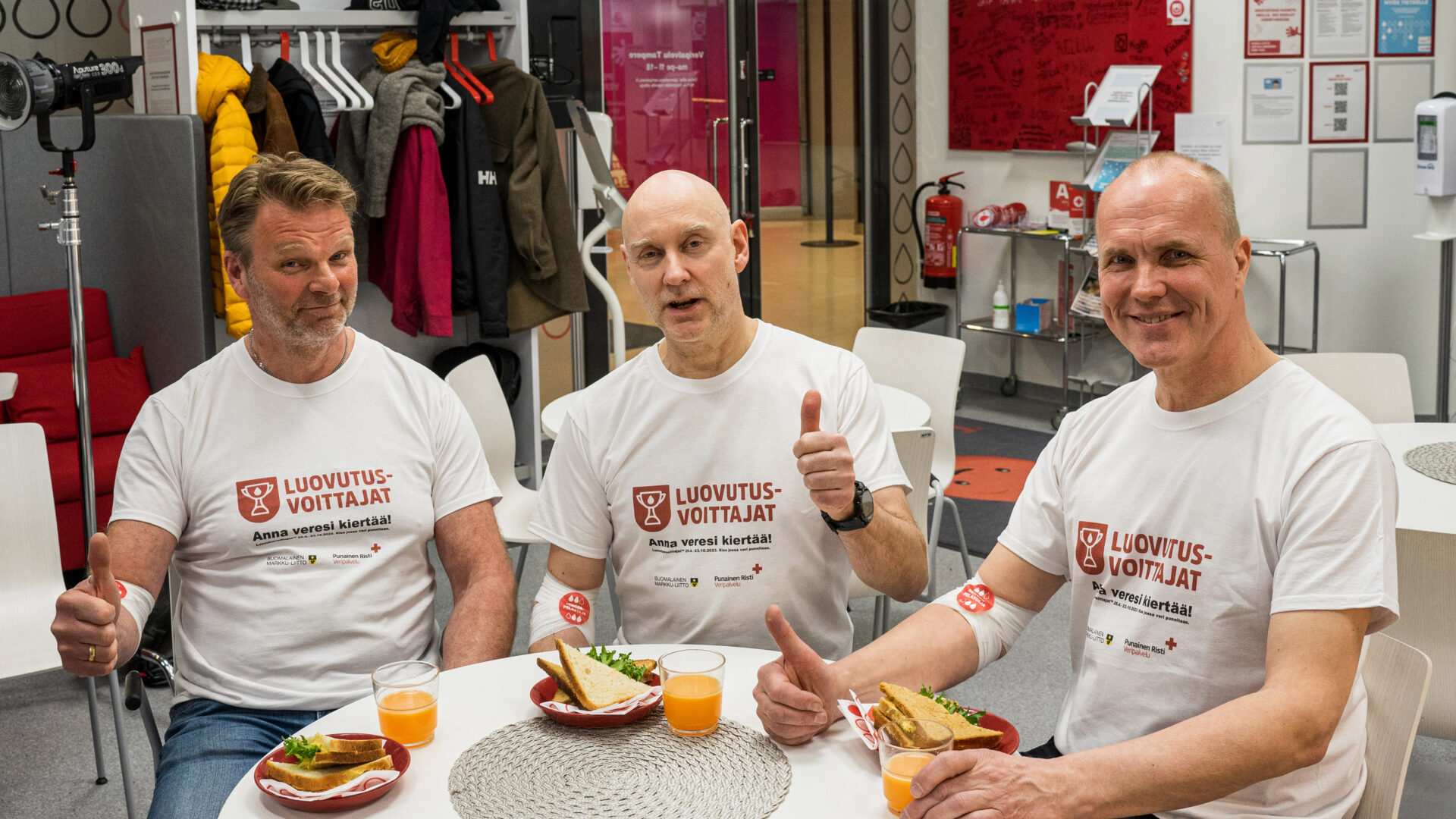 Kolme Markkua kahvittelemassa verenluovutuksen jälkeen. Kaikilla valkoiset t-paidat, joissa Luovutusvoittajat-logo.