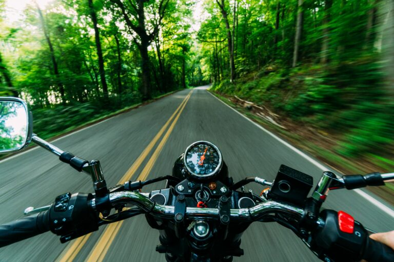 Moottoripyöräilijä ajaa asfalttitiellä, molemmin puolin näkyy vihreää metsää. Kuvakulma ajajan.
