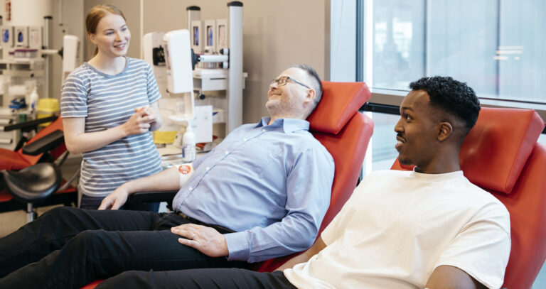 Kaksi miestä istuu verenluovutuksessa ja juttelee Veripalvelun hoitajan kanssa.