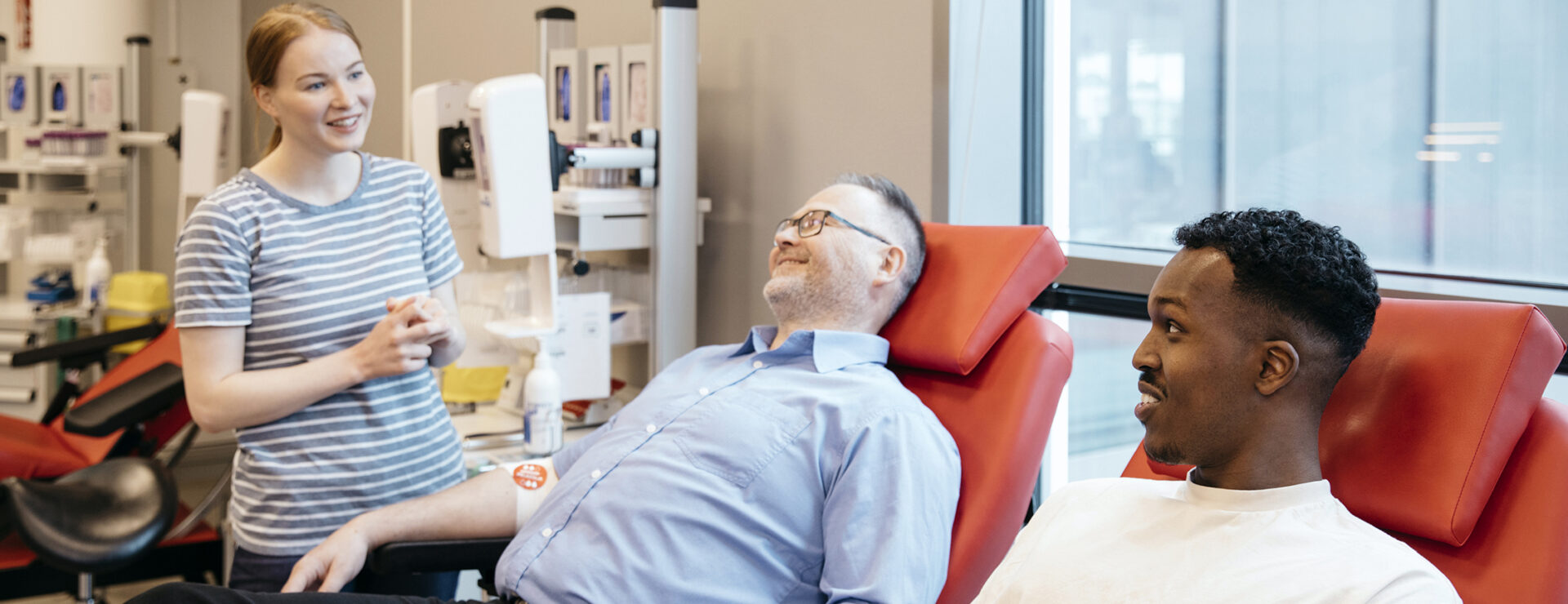 Kaksi verenluovuttajaa istuu luovutuspedeillä ja keskustelee hymyillen Veripalvelun hoitajan kanssa.