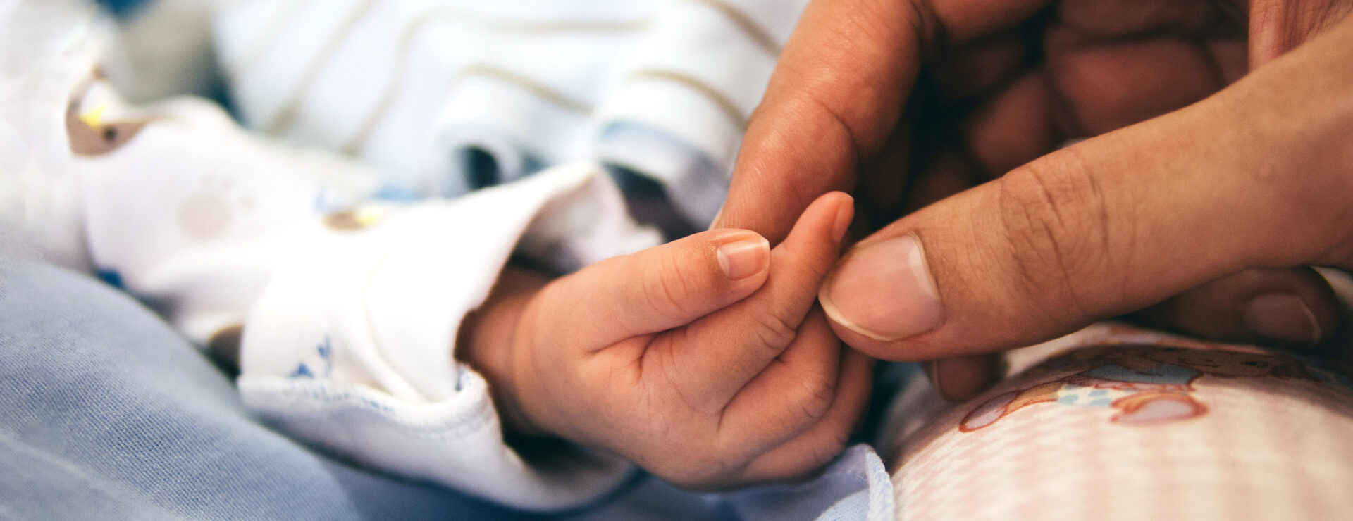 Adult holding baby's hand.