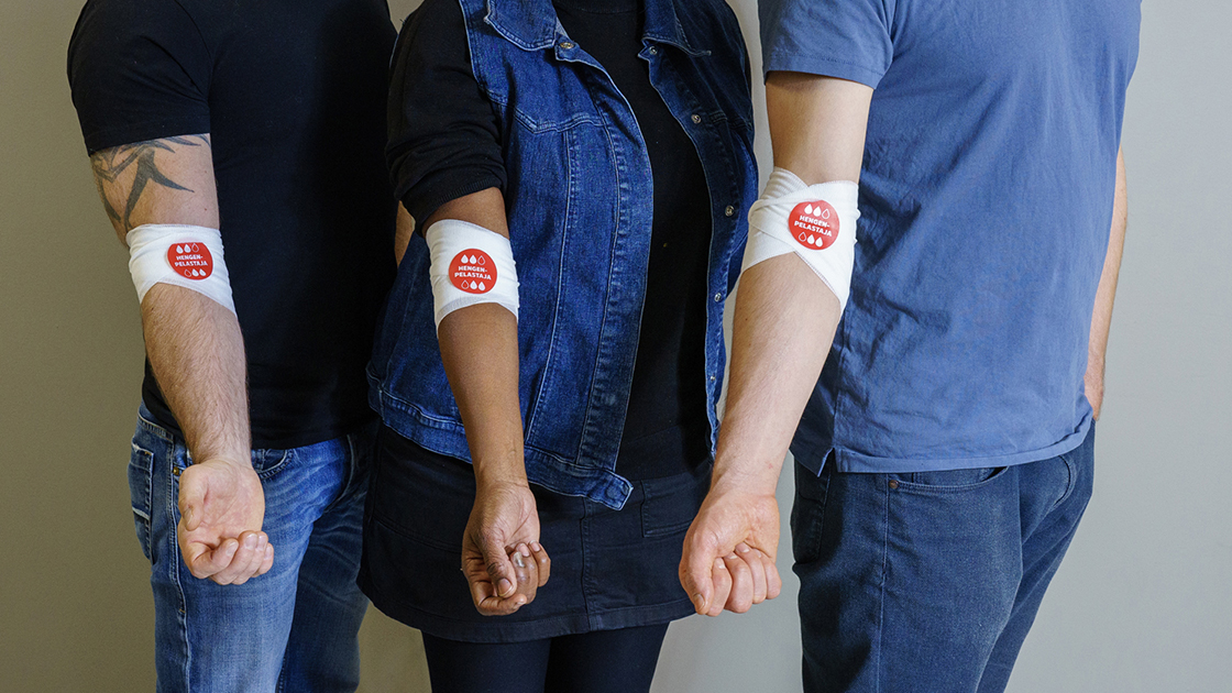 Kolme henkilöä rivissä, käsivarsissa sideharso ja verenluovuttajan Hegenpelastaja-tarra.