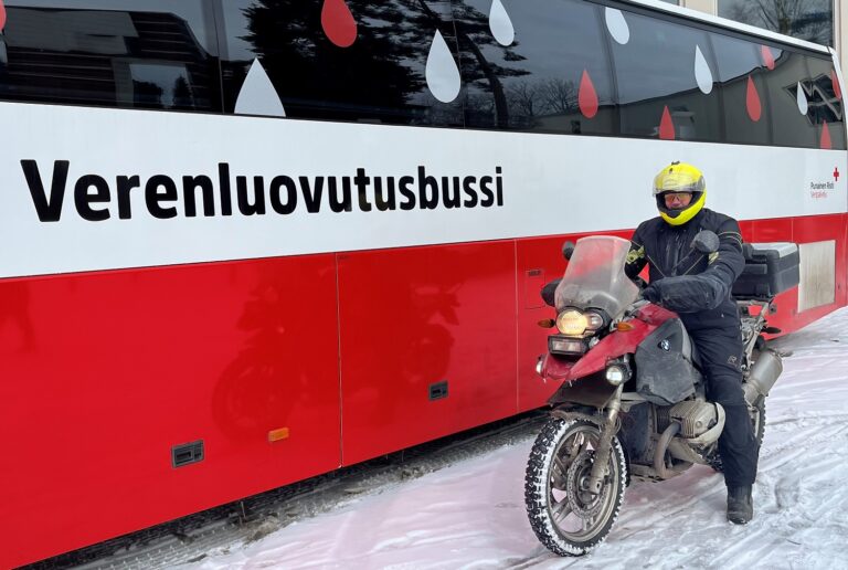Verenluovuttaja Raimo Ryhtä moottoripyörän selässä Verenluovutusbussin vieressä.