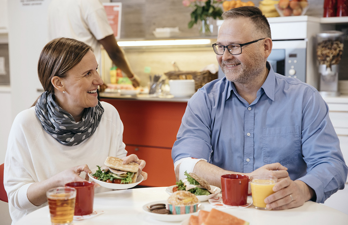 Två blodgivare sitter glatt med kaffe och ett mellanmål i donationsställets cafeterian.