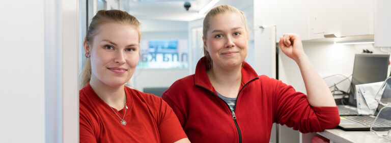 Kaksi Veripalvelun punapaitaista hoitajaa hymyilee kameralle Verenluovutusbussissa.