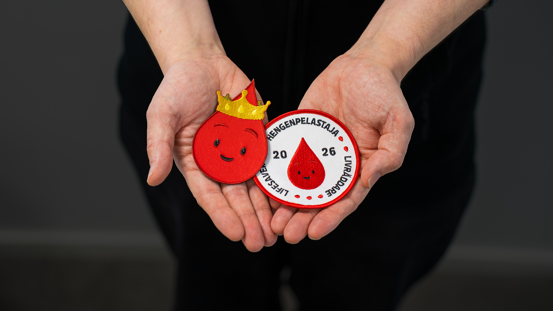 Ihminen pitää käsissään kahta Veripalvelun haalarimerkkiä