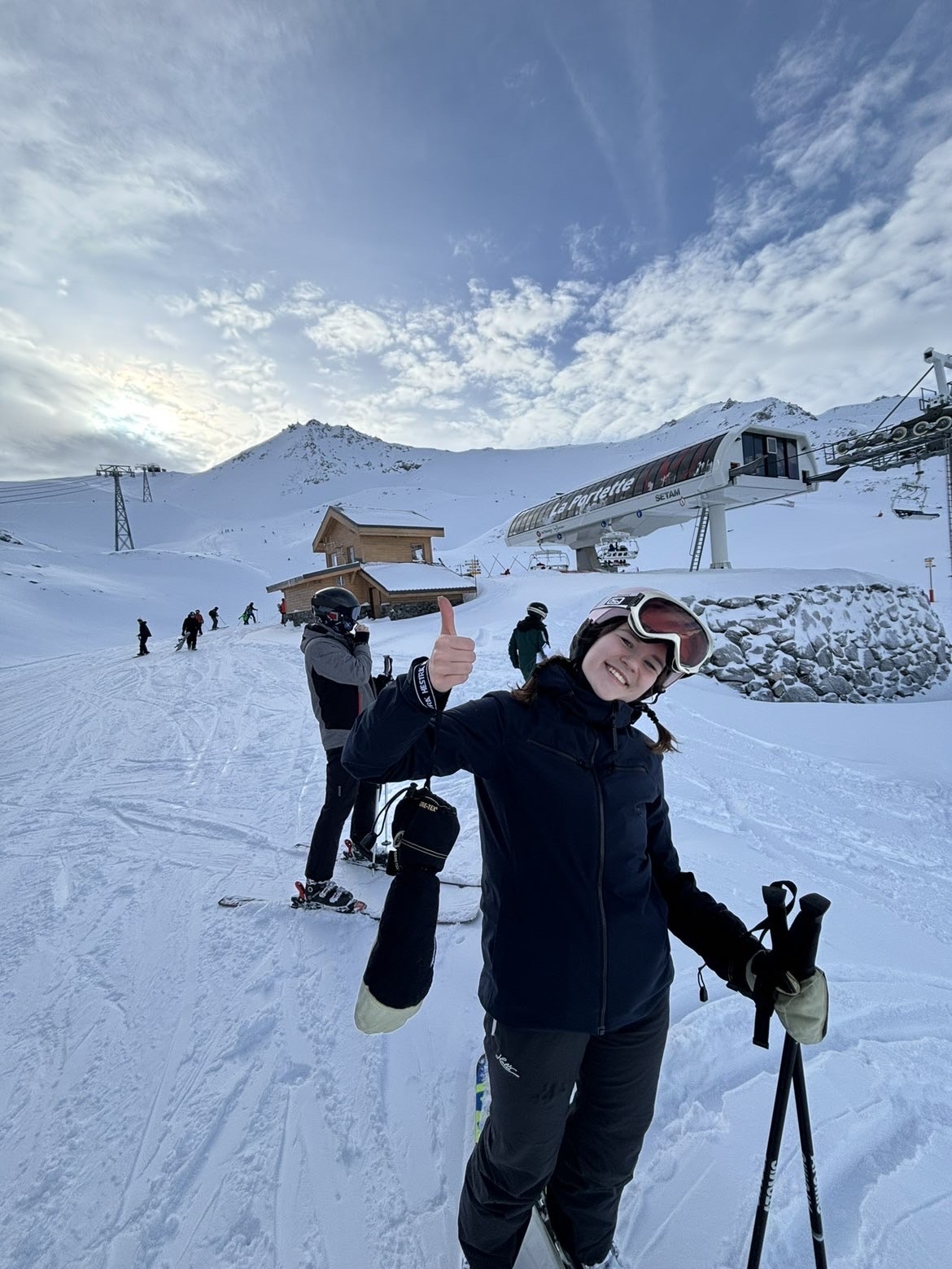 Nainen näyttää peukkua ja hymyilee laskettelurinteessä.