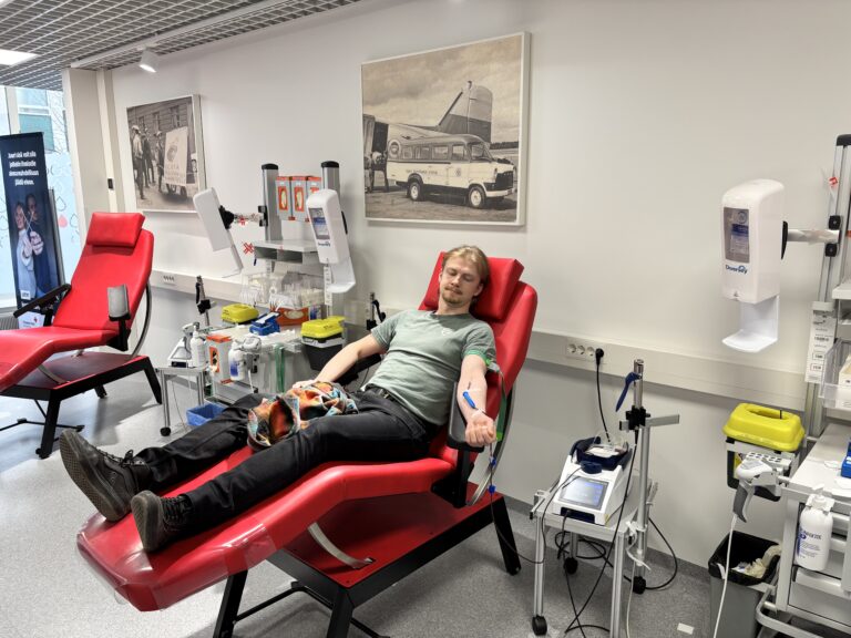 Nuori mies makaa punaisella tuolilla eli luovutuspedillä Veripalvelun toimipisteessä harmaata taustaa vasten.