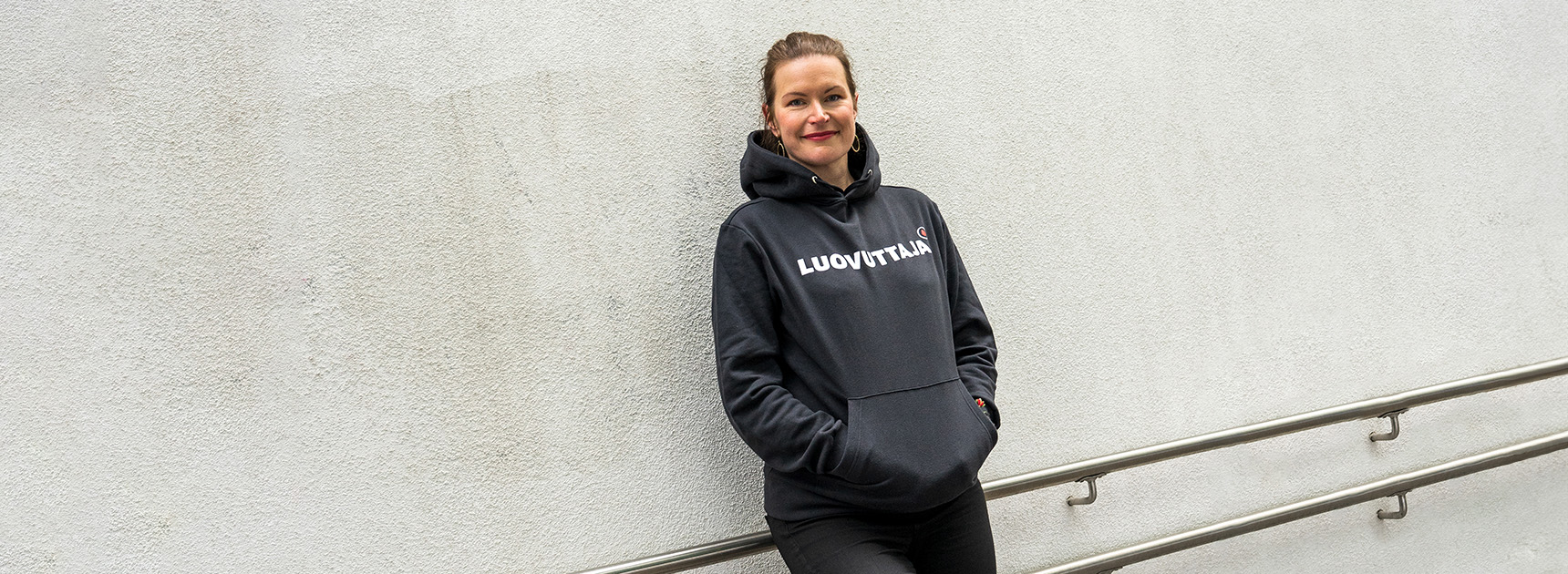 A person wearing the Donor hoodie leaning against a concrete wall.