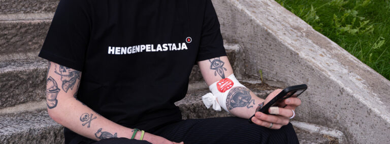 En blodgivare iklädd en ‘Livräddare’-T‑tröja som använder en app.